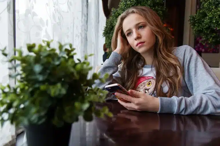 A young woman in deep contemplation, holding her phone.