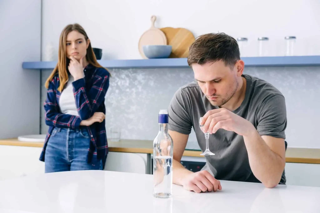 Man drinking in kitchen with wife watching, illustrating how alcohol consumption worsens mental health